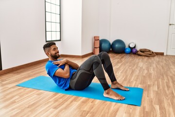 Fototapeta na wymiar Handsome hispanic man doing exercise and stretching on yoga mat, practicing flexibility and training at the gym