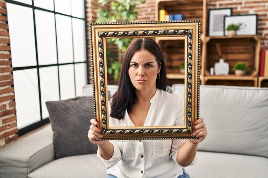 Young hispanic woman holding empty frame skeptic and nervous, frowning upset because of problem. negative person.
