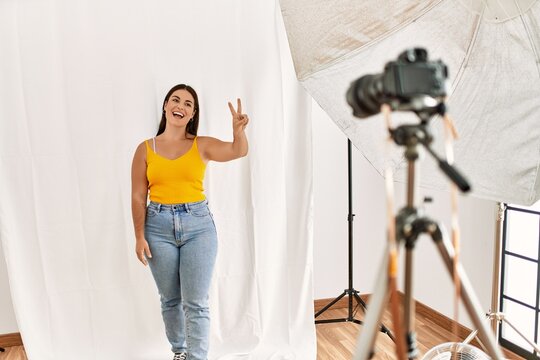 Young beautiful hispanic woman posing as model at photography studio showing and pointing up with fingers number two while smiling confident and happy.