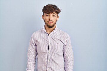 Arab man with beard standing over blue background relaxed with serious expression on face. simple and natural looking at the camera.