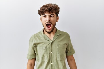 Young arab doctor man standing over isolated background angry and mad screaming frustrated and furious, shouting with anger. rage and aggressive concept.