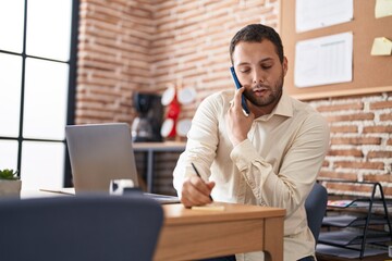 Young man business worker talking on smartphone writing on reminder paper at office