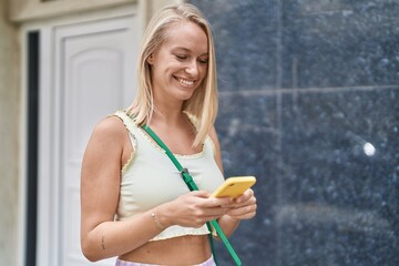 Young blonde woman smiling confident using smartphone at street