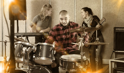Group of young musicians with expressive male drummer rehearsing in rehearsal room