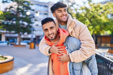 Two man couple hugging each other holding boyfriend on back at park