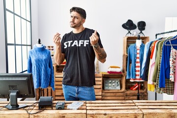 Young hispanic man working at retail boutique doing money gesture with hands, asking for salary...