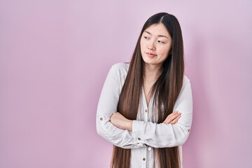 Fototapeta premium Chinese young woman standing over pink background looking to the side with arms crossed convinced and confident