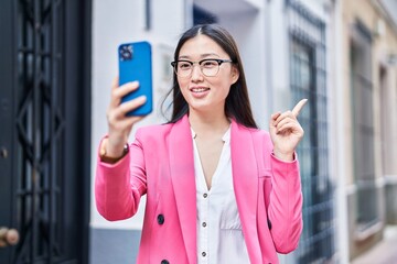 Chinese young woman doing video call with smartphone smiling happy pointing with hand and finger to the side