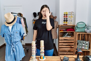 Young asian woman working as manager at retail boutique covering one eye with hand, confident smile on face and surprise emotion.