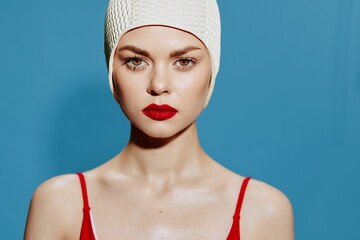 Serious tense woman in swimming cap red swimsuit on blue background looking at camera