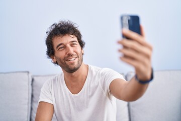 Young hispanic man make selfie by smartphone sitting on sofa at home