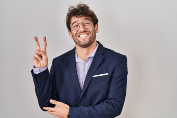 Hispanic business man wearing glasses smiling with happy face winking at the camera doing victory sign. number two.