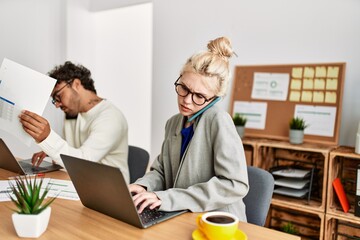 Obraz premium Two business workers talking on the smartphone and using laptop at the office.