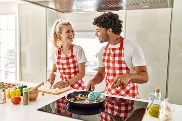 Young couple smiling happy cooking using frying pan at kitchen.