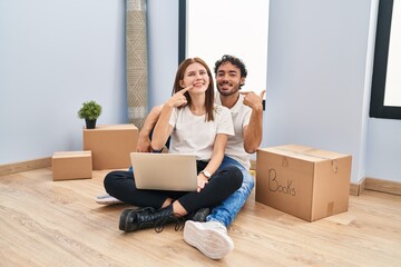 Young couple using laptop at new home smiling cheerful showing and pointing with fingers teeth and mouth. dental health concept.