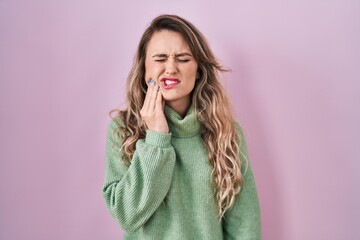 Young caucasian woman standing over pink background touching mouth with hand with painful expression because of toothache or dental illness on teeth. dentist