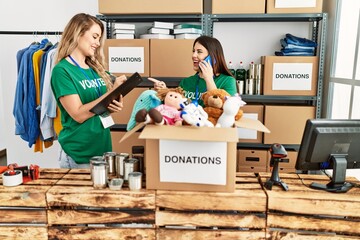 Two young volunteers woman smiling happy working at charity center. Girl smiling happy talking on the smartphone.