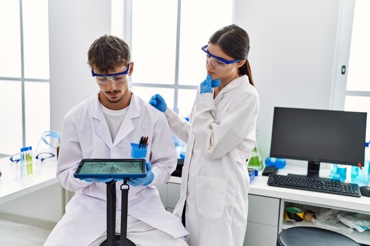 Man and woman partners wearing scientist uniform using touchpad with embryo image at laboratory