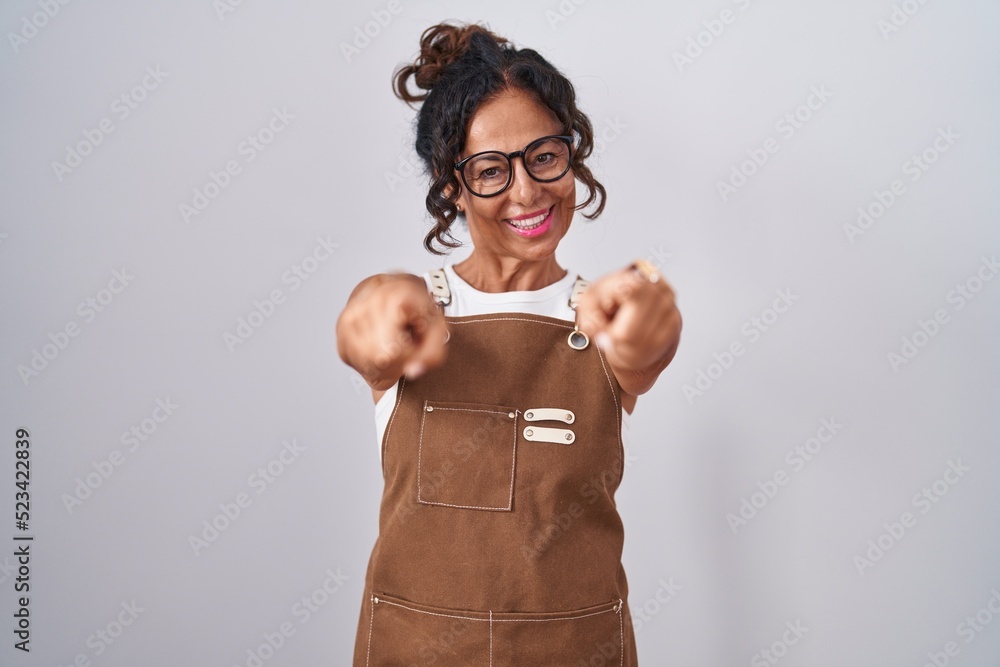 Sticker Middle age woman wearing apron over white background pointing to you and the camera with fingers, smiling positive and cheerful