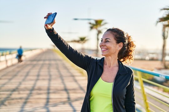 Middle age hispanic woman working out taking selfie picture at promenade