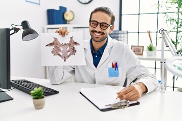 Obraz premium Handsome hispanic man working as psychologist showing rorschach test at professional clinic