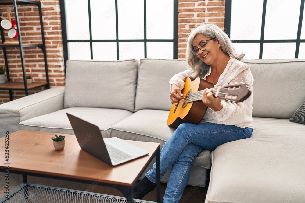 Wall mural Middle age woman having online guitar class at home