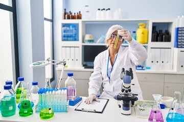 Middle age woman wearing scientist uniform holding test tube at laboratory