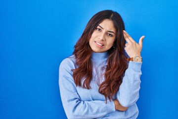 Hispanic young woman standing over blue background shooting and killing oneself pointing hand and fingers to head like gun, suicide gesture.