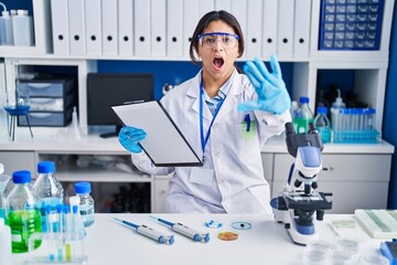 Hispanic young woman working at scientist laboratory doing stop gesture with hands palms, angry and...