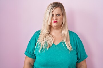 Caucasian plus size woman standing over pink background skeptic and nervous, frowning upset because...