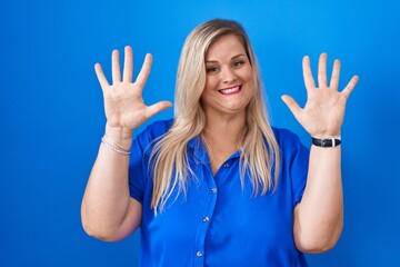 Fototapeta premium Caucasian plus size woman standing over blue background showing and pointing up with fingers number ten while smiling confident and happy.