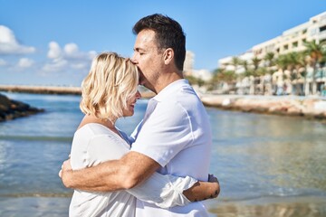 Fototapeta na wymiar Middle age man and woman couple hugging each other and kissing standing at seaside