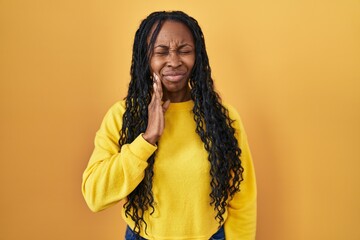African woman standing over yellow background touching mouth with hand with painful expression because of toothache or dental illness on teeth. dentist