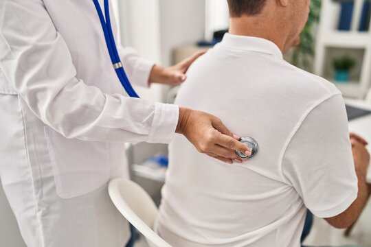 Middle age man and woman doctor and patient auscultating pulmonary sound having medical consultation at clinic