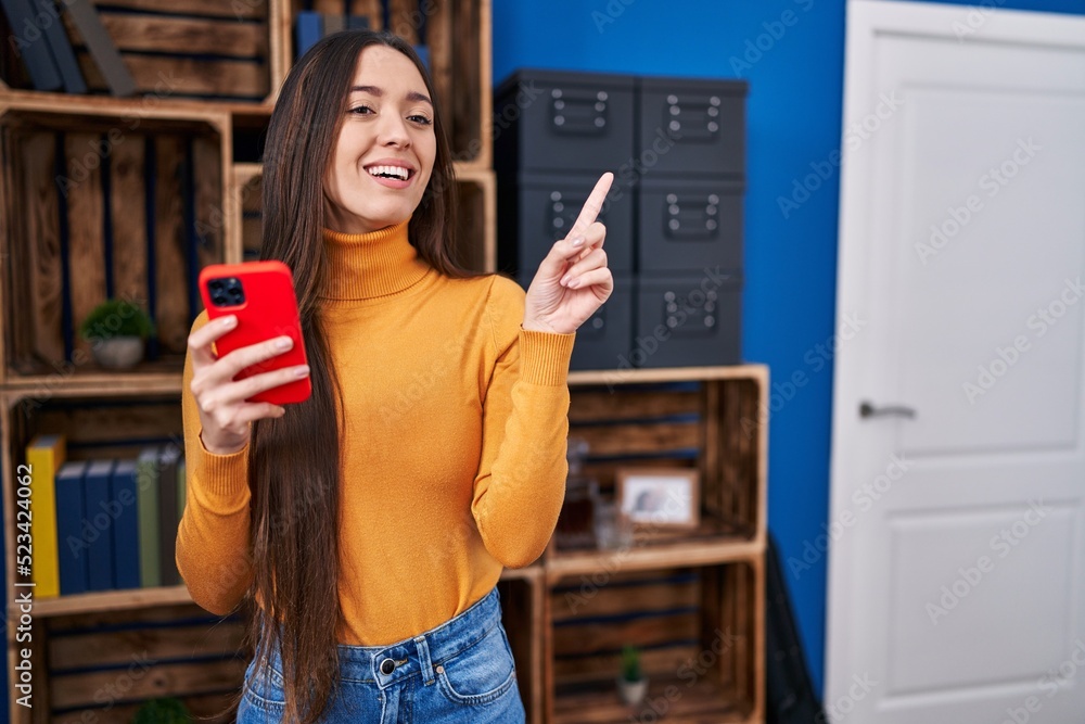 Sticker young brunette woman using smartphone smiling happy pointing with hand and finger to the side