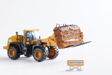 Road sign that says confectionery next to toy forklift carrying piece of chocolate biscuit cake....