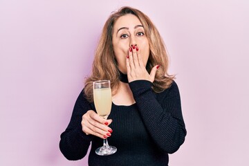 Middle age caucasian woman drinking glass of champagne covering mouth with hand, shocked and afraid...