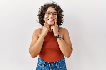 Young hispanic woman wearing glasses standing over isolated background smiling with open mouth, fingers pointing and forcing cheerful smile