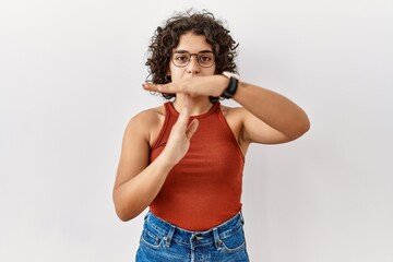 Young hispanic woman wearing glasses standing over isolated background doing time out gesture with...