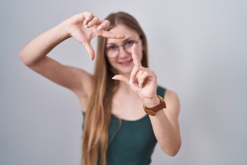 Fototapeta premium Young caucasian woman standing over white background smiling making frame with hands and fingers with happy face. creativity and photography concept.