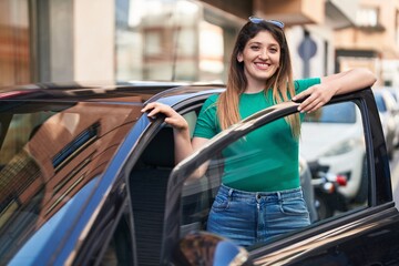 Young hispanic woman smiling confident leaning on door car at street