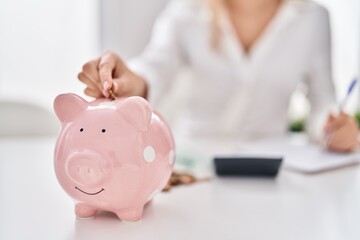 Young woman inserting coin on piggy bank at home