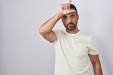 Hispanic man with beard standing over isolated background making fun of people with fingers on...