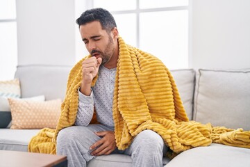 Young hispanic man sitting on sofa coughing at home