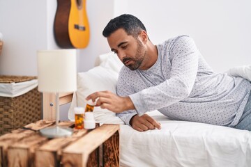 Fototapeta na wymiar Young hispanic man lying on bed holding pills at bedroom