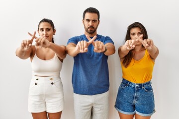 Group of young hispanic people standing over isolated background rejection expression crossing fingers doing negative sign - obrazy, fototapety, plakaty
