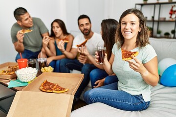 Group of young hispanic friends smiling happy eating italian pizza sitting on the sofa at home.