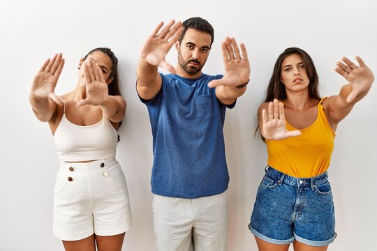 Group of young hispanic people standing over isolated background doing frame using hands palms and fingers, camera perspective