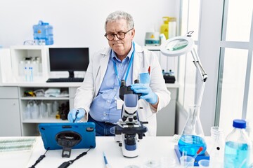 Fototapeta premium Middle age grey-haired man wearing scientist uniform using microscope and touchpad at laboratory
