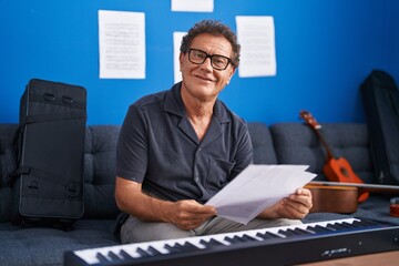 Middle age man musician smiling confident reading music sheet at music studio